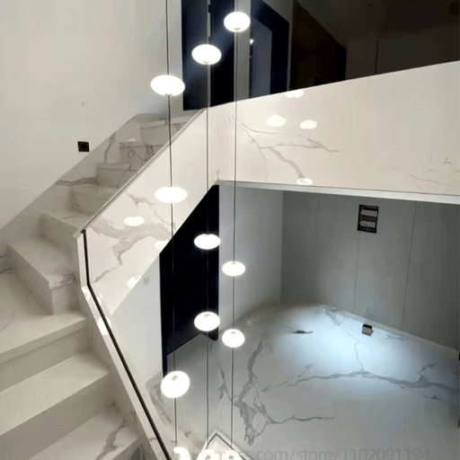 Modern multi-tier LED chandelier illuminating a marble staircase.