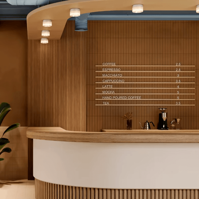 Modern cafe interior with wooden counter and menu board displaying coffee and tea options, featuring contemporary lighting fixtures.