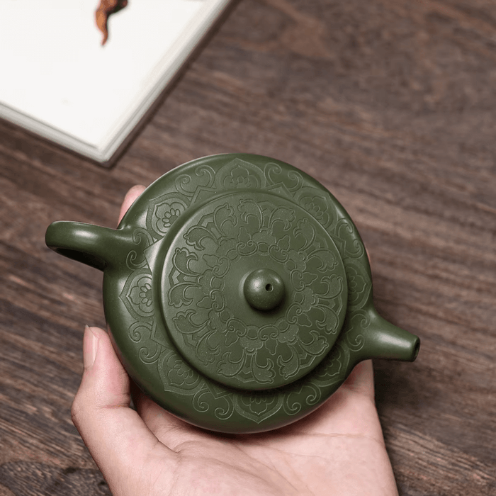 Handmade green Yixing clay teapot with intricate design, held in hand, showcasing traditional Chinese Zisha tea ware craftsmanship.