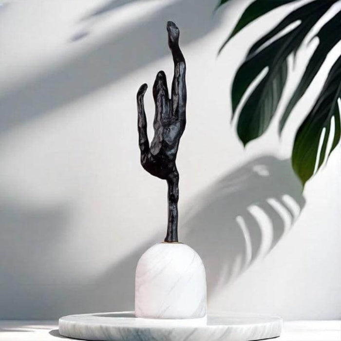 Giacometti inspired abstract metal sculpture on marble base with shadow and leaf in background, modern home decor piece.