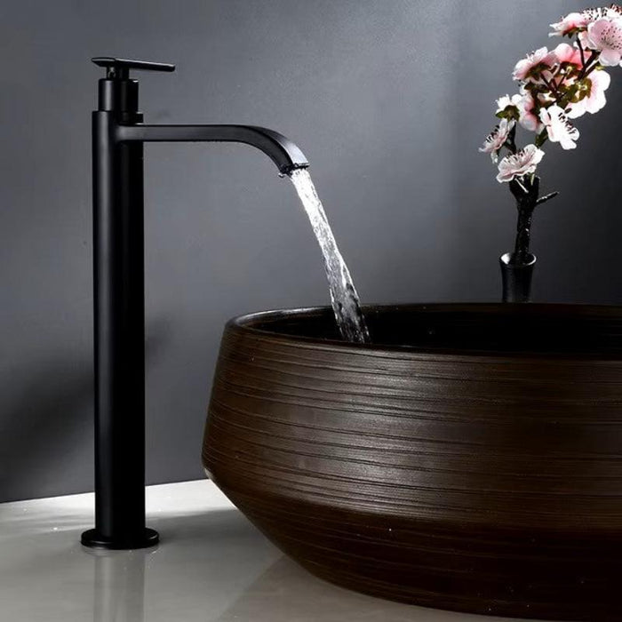 Tall wall-mount cold water basin faucet in sleek black design with flowing water into a wooden sink, modern bathroom fixture.