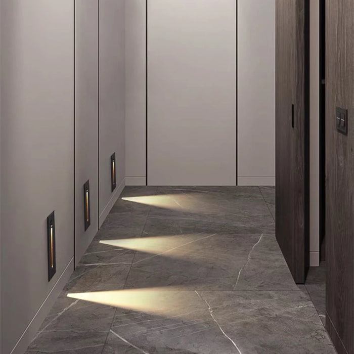 Modern hallway with installed indoor LED wall lamps providing warm, focused lighting along a sleek, stone floor walkway.