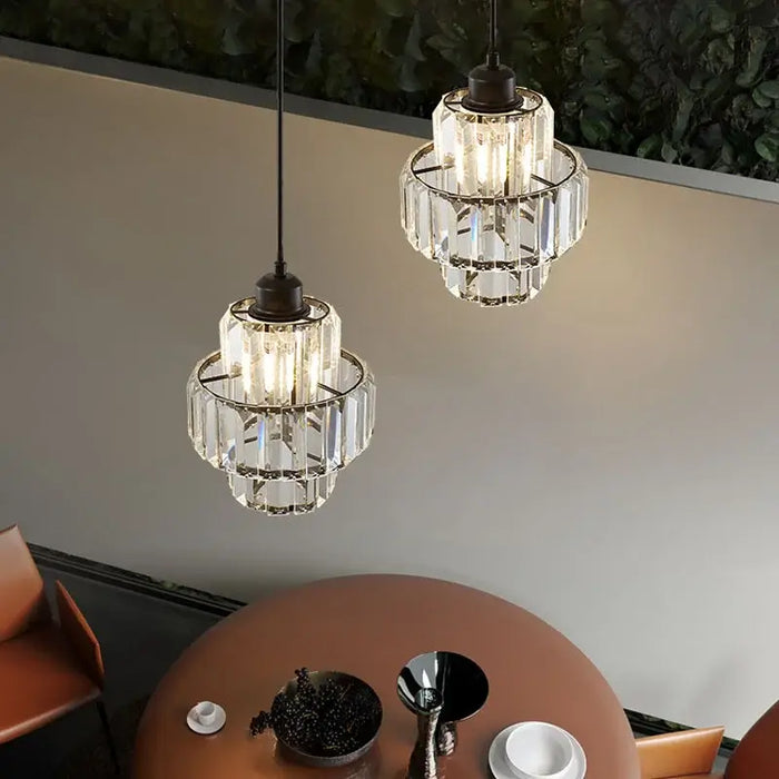 Elegant tiered crystal glass pendant lights hanging over a modern dining table, providing warm LED illumination.