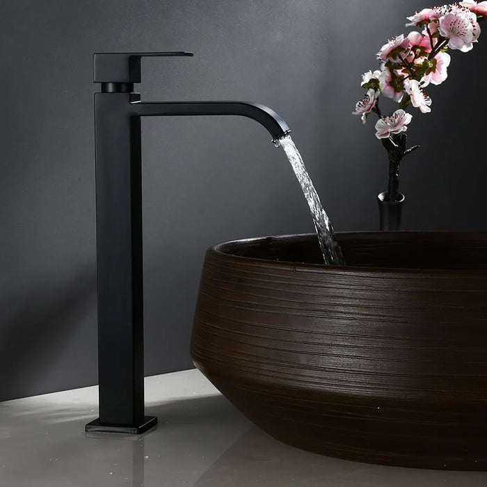 Tall wall-mount cold water basin faucet with sleek design, flowing into a modern wooden basin in a minimalist bathroom setting.