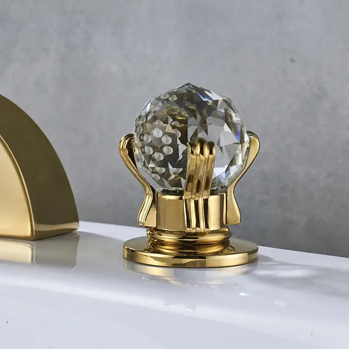 Elegant crystal handle on a golden base of a waterfall faucet, adding luxury to bathroom decor with polished chrome accents.