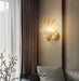 Modern luxury brass shell wall lamp with clear glass shade illuminating a living room with elegant decor.