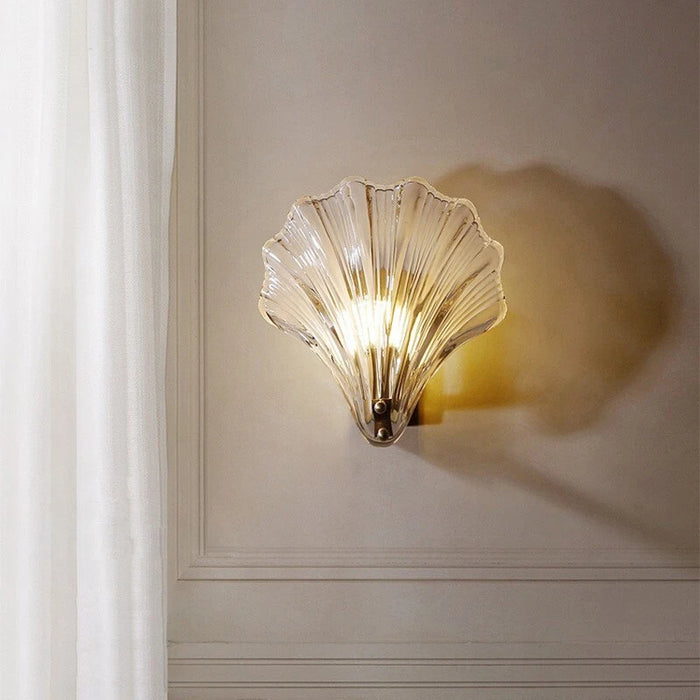 Modern luxury brass shell wall lamp with clear glass shade on elegant interior wall.