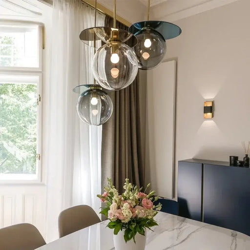 Modern pendant lamp with elegant colored glass orbs above dining table, featuring artistic lighting in a contemporary room setting.