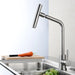 Stainless steel rotary kitchen mixer faucet with brushed finish installed above a sink next to fruits and a cutting board.