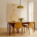 Stylish dining room with retro glass pendant light, wooden table, yellow chairs, and modern wall art.