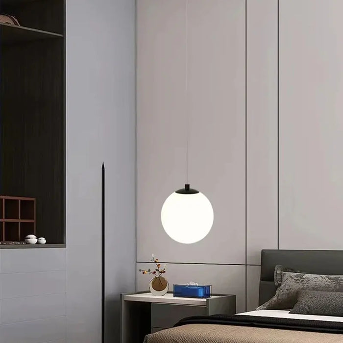 Modern round glass pendant light illuminating a stylish bedroom interior.