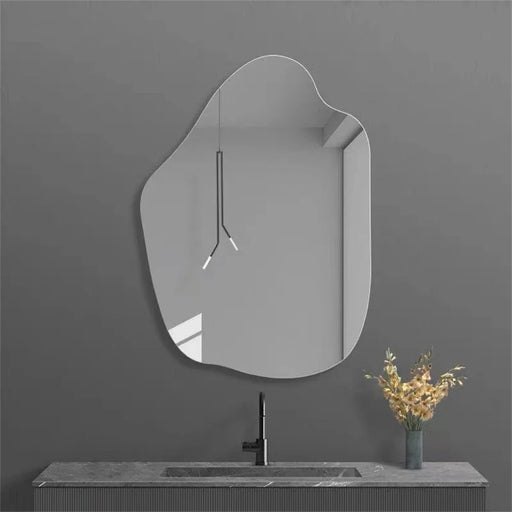 Irregular acrylic bathroom mirror with polished edges mounted on a gray wall above a modern sink.