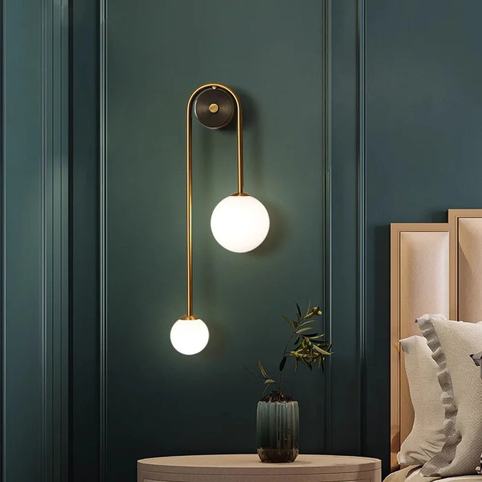 Modern glass ball golden LED wall sconce illuminating a chic bedroom setting.