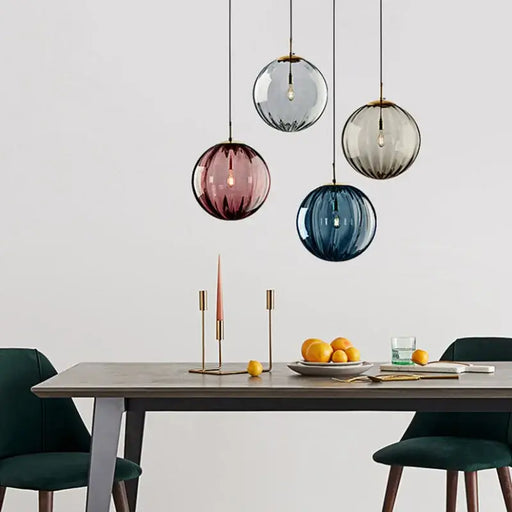 Vibrant colored glass ball pendant lights in red, blue, gray, and brown hanging over a dining table with modern decor.