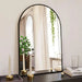 Large arch mirror with modern aluminum frame reflecting a bright room setting with plants and candles.