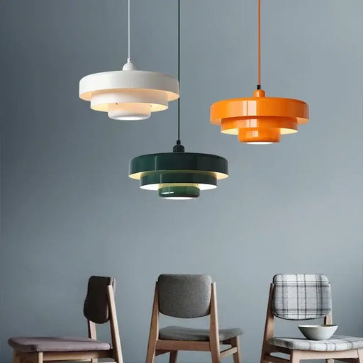 Danish Modern LED Pendant Lighting in orange, dark green, and white hanging over chairs in a stylish, minimalistic room.