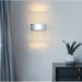 Modern LED acrylic wall lamp with Nordic design illuminating a stylish interior space with a plant and grey curtains.