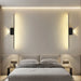 Modern long strip wall lamp with LED lighting, CE certified, wall-mounted above bed, illuminating cozy bedroom space.