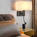 Modern bedside wall lamp with USB port and spotlight, illuminating bedroom, phone charging on nightstand.