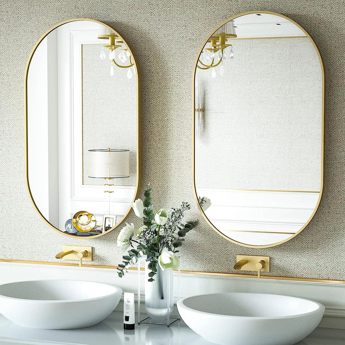 Oval wall-mounted mirror with gold frame in modern bathroom setting featuring double sinks and decorative elements.