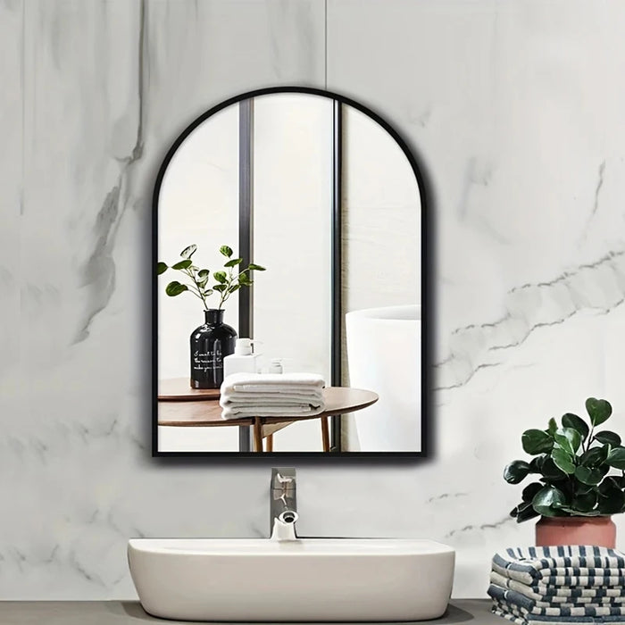 Large arched mirror with aluminum frame in modern bathroom setting, reflecting a table with plants and folded towels.