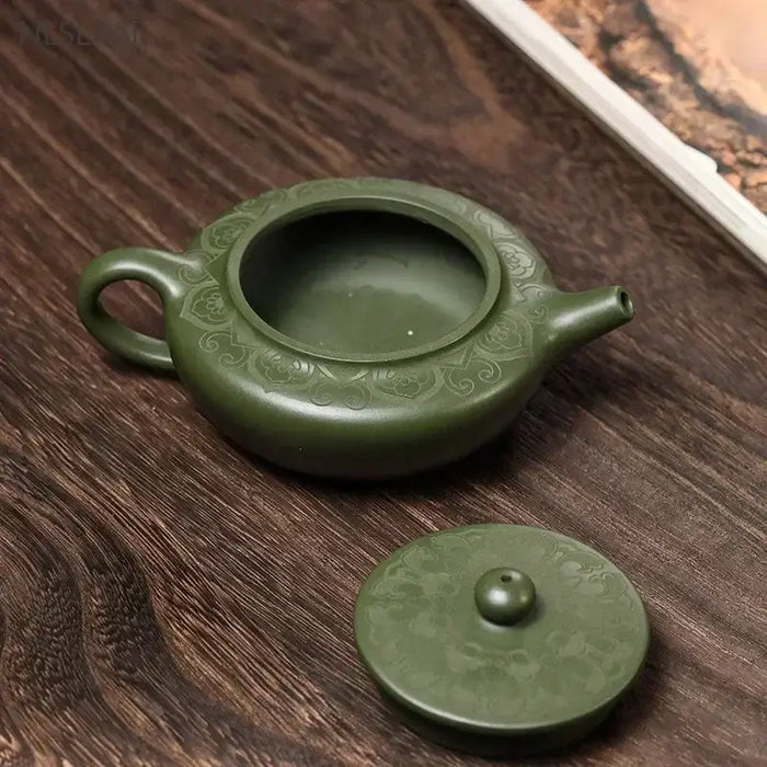 Handmade green Yixing clay teapot with lid on wooden surface, showcasing traditional Chinese Zisha tea ware craftsmanship.