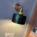 Vintage glass wall lamp with green stained glass shade, installed on a blue wall, illuminating a cozy interior space.