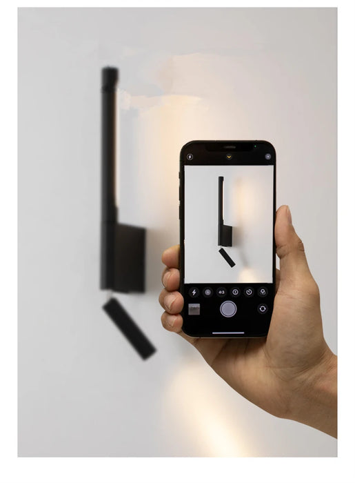 Modern adjustable bedside wall lamp with LED light captured on smartphone, highlighting sleek black design and wall-mounted style.