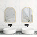 Large arch mirrors with gold frames in a modern bathroom setting above round white sinks.