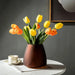 Elegant brown vase with vibrant yellow and orange tulips on a white table beside a coffee cup.