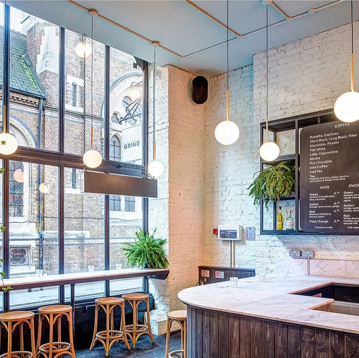 Modern coffee shop interior with pendant lighting, bar stools, and large windows creating a bright and inviting atmosphere.