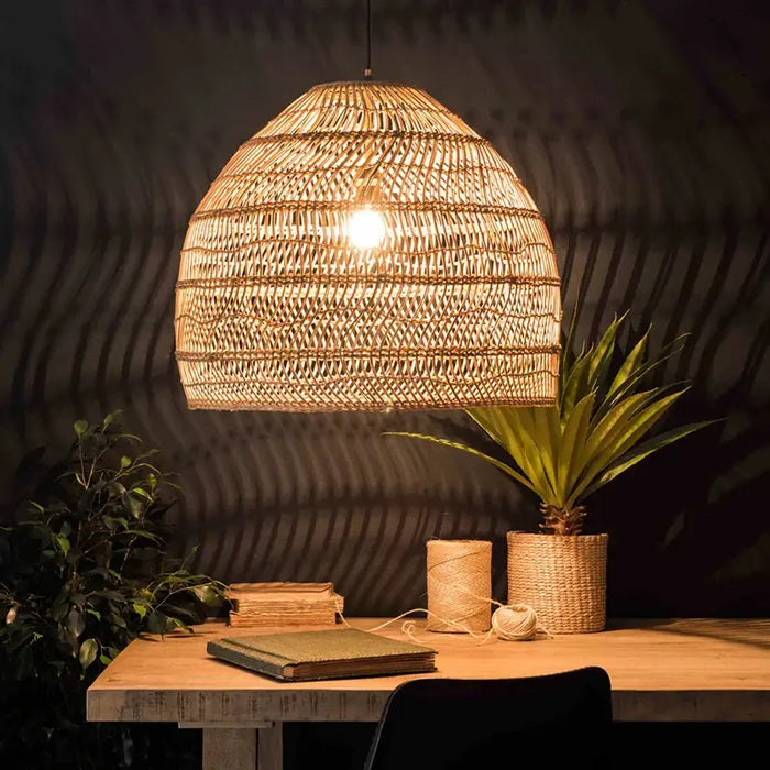 Handwoven bamboo pendant light illuminating a stylish wooden desk with plants and books in a cozy room setting.