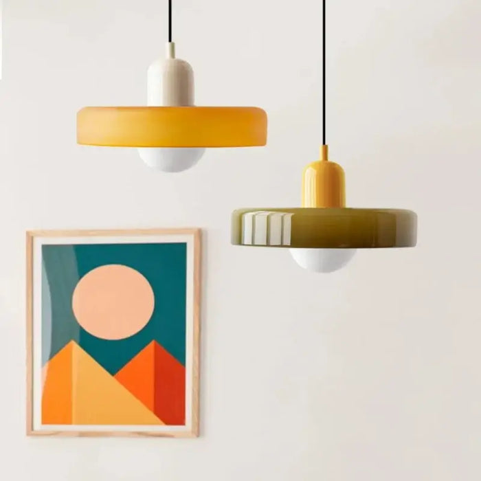 Retro glass pendant lights in orange and olive colors hanging beside framed abstract art on white wall.