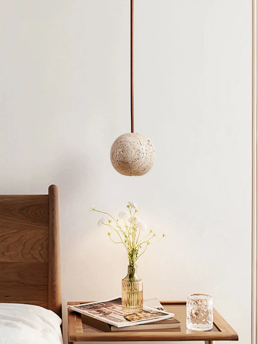 Nordic Round Travertine LED Pendant Light hanging over a bedside table with a vase and book.