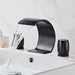 Modern wave shape waterfall basin faucet set in black with serene water flow in a stylish bathroom sink.