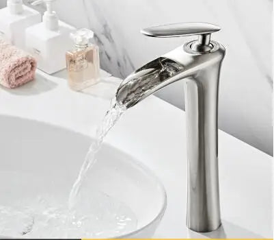 Elegant waterfall basin mixer faucet in chrome finish, flowing water into a white basin in a modern bathroom setting.