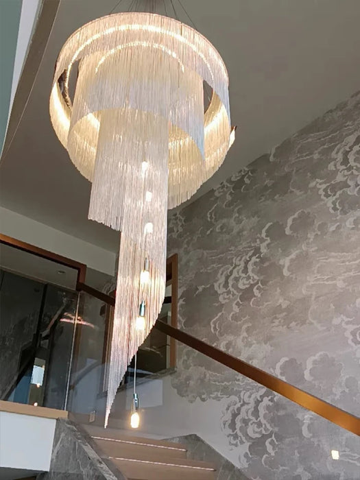 Modern loft spiral chandelier with golden tassels hanging over a staircase.