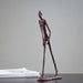 Bronze Giacometti-inspired walking man sculpture with elongated limbs on a table.