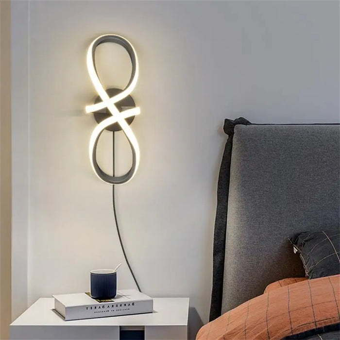 Modern artistic wall lamp with infinity design above a nightstand, featuring a warm LED glow, crafted from aluminum and wood.