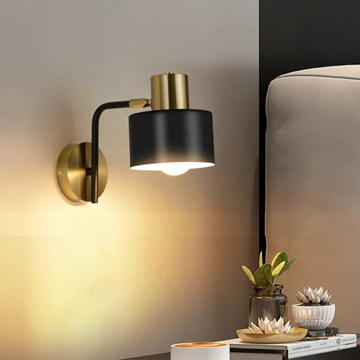 Modern sleek wall light with black and brass finish in bedroom setting, illuminating side table with decor.