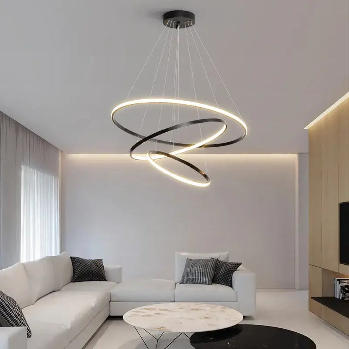 Modern LED multi-ring chandelier illuminating a stylish living room with white sofa and marble table.