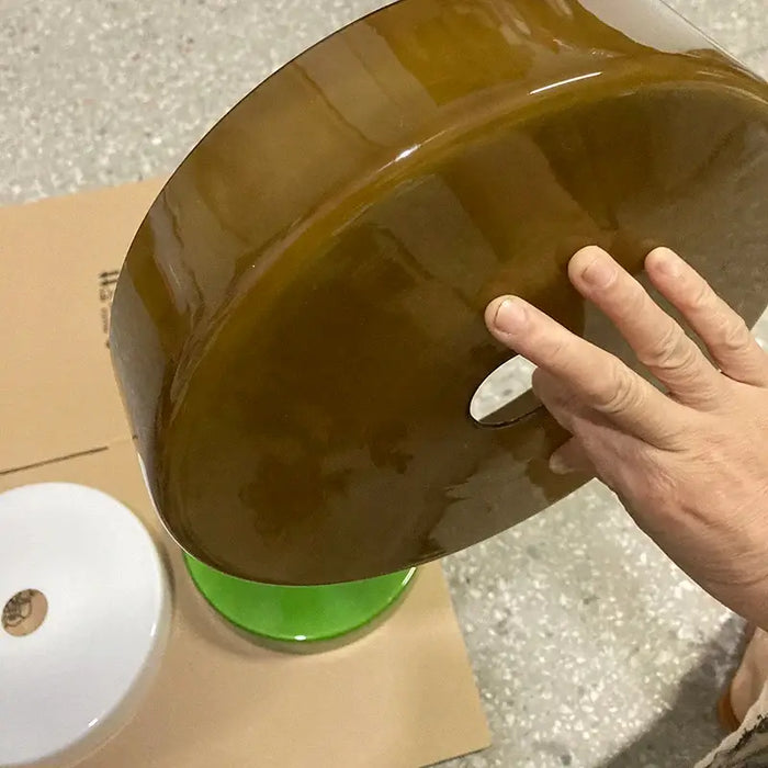 Person holding a brown Retro Glass Pendant Light shade with green and white shades nearby on a floor.