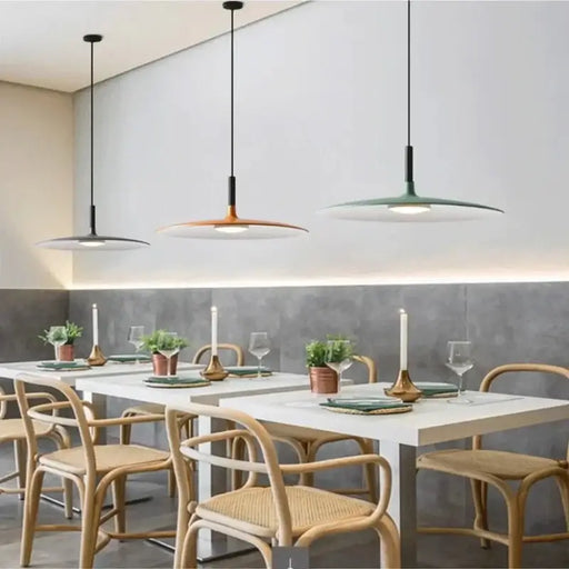 Modern round flat dish pendant lights over dining table with wooden chairs and minimalist decor.