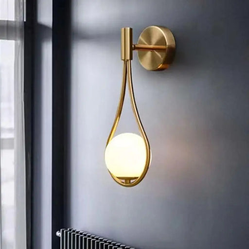 Nordic Elegance Drop Wall Lamp in gold finish with LED bulb, mounted on dark wall, showcasing modern design with frosted glass shade.