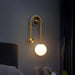 Golden LED wall sconce with frosted glass ball shade illuminating a modern bedroom setting.