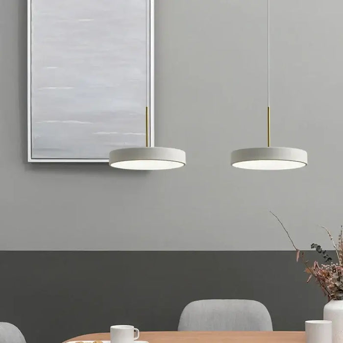 Modern LED saucer pendant lights hanging above a dining space with minimalist decor.