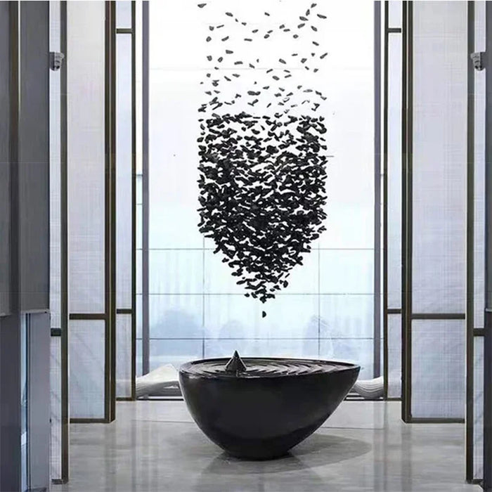 Modern art installation with black particles hovering over a sleek black bowl in a minimalist indoor setting.