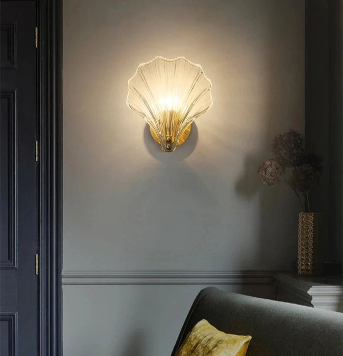 Modern luxury brass shell wall lamp with clear glass shade illuminating elegant home interior.