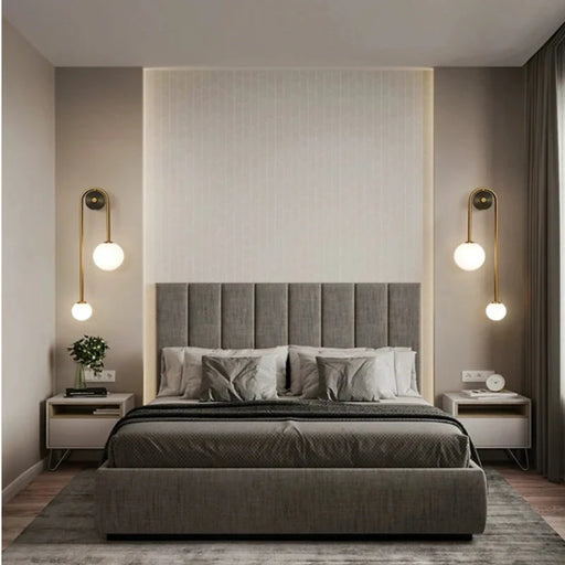 Modern bedroom with grey bed and gold LED wall sconces featuring frosted glass ball lights on either side.