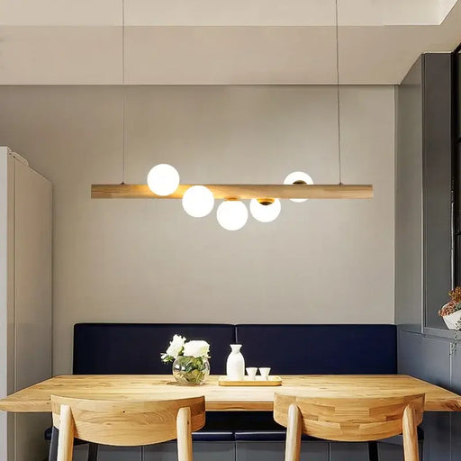 Modern minimalist strip chandelier with wooden beam and orbs of light above a dining table in a stylish room.